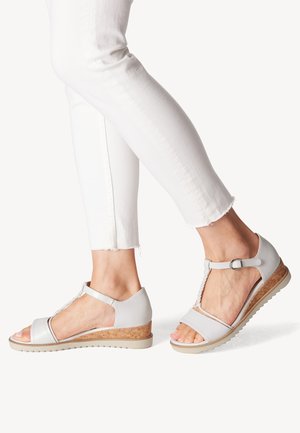 Lys grå sandaler med en kork kilehæl, åben tå, T-strop design, tekstureret detaljering og justerbar ankelrem.