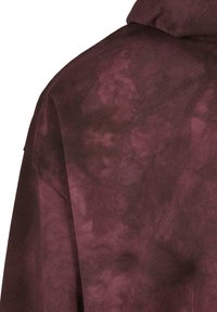 Hanorac burgundiu, realizat dintr-un material moale și texturat, cu un model tie-dye. Designul include o croială largă și glugă.