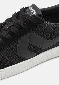 Schwarze Sneaker mit einem strukturierten Obermaterial aus Stoff, Wildlederakzenten und einer weißen Gummisohle; ausgestattet mit schwarzen Schnürsenkeln und Branding auf der Zunge.