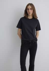 Black cotton t-shirt with short sleeves, round neckline, and a relaxed fit. Paired with dark denim jeans. Plain design, no visible patterns.