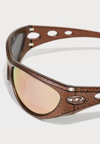 Óculos de sol castanhos com um padrão salpicado, lentes espelhadas e um design de recorte distinto. Logotipo exibido na lateral.