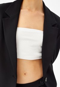 Svart kavaj med slag över en vit ribbad bandeau-top. Kavajen har en enkel knappstängning och en slät yta.