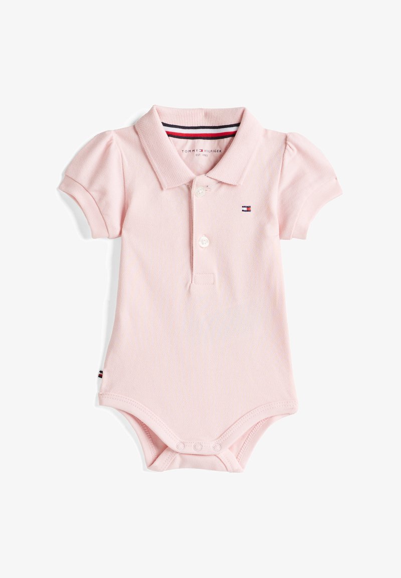 Světle růžový polo overal z texturované látky, s knoflíkovým límcem, krátkými vystouplými rukávy a detailem loga na hrudi. Zapínání na patentky na spodní části.