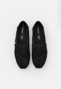 Para czarnych, koronkowych butów slip-on TOMS z kwiatowym wzorem, rozmiar W6, wyeksponowana na jednolitym białym tle.