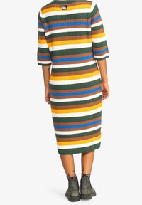 Vestido de punto acanalado hasta la rodilla con rayas horizontales en verde, amarillo, blanco, azul y marrón, combinado con botas hasta el tobillo de color gris oscuro.