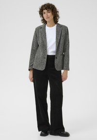 Szary, fakturalny blazer na białej koszuli, w połączeniu z czarnymi, sztruksowymi spodniami o szerokich nogawkach i czarnymi butami. Prosty design z pojedynczym zapięciem na guzik.