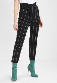 Černobílé pruhované kalhoty s vysokým pasem a látkovým páskem, s tapered leg designem. Nosené s tyrkysovými kotníkovými botami.