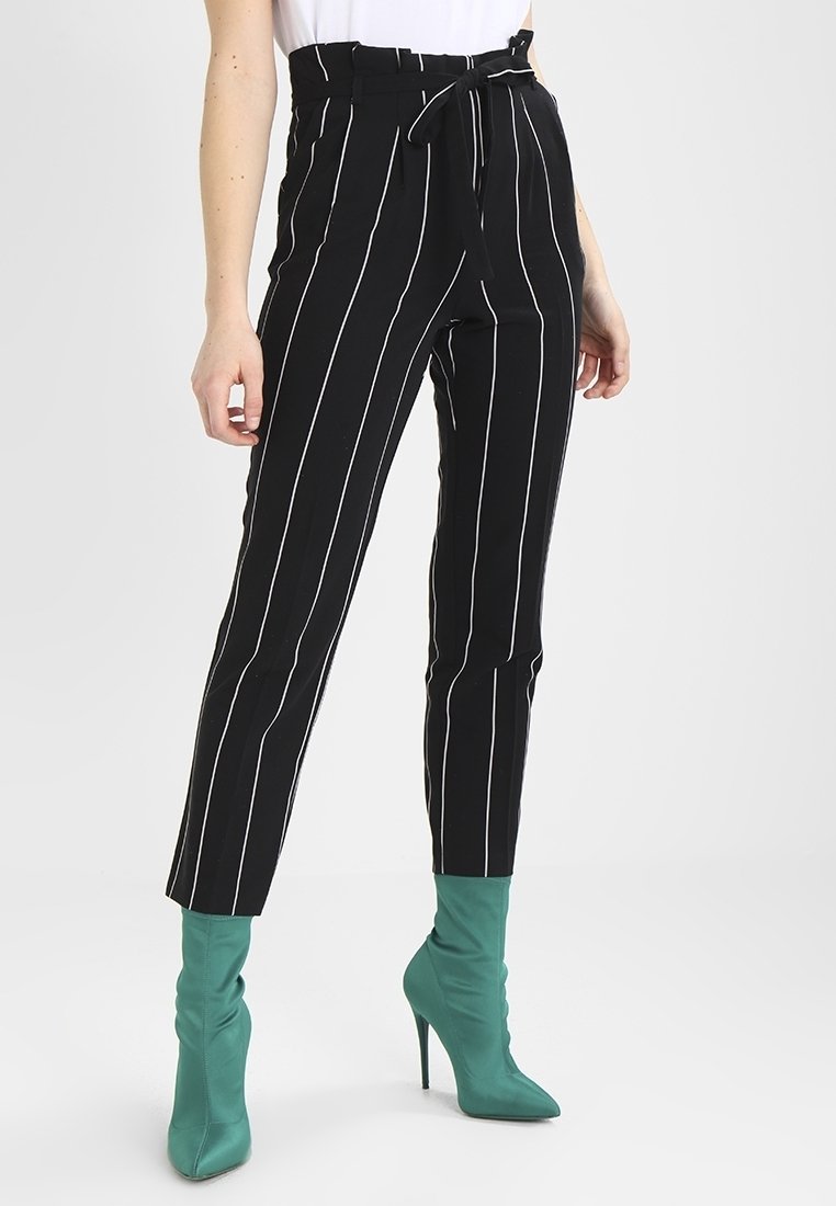 Černobílé pruhované kalhoty s vysokým pasem a látkovým páskem, s tapered leg designem. Nosené s tyrkysovými kotníkovými botami.