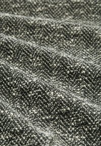 Gestructureerde stof met een visgraatpatroon in zwart en wit, met een zachte, geweven uitstraling en een gespikkeld effect.
