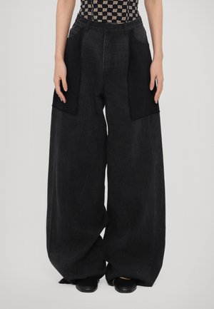 Pantalones de mezclilla negros de pierna ancha con paneles de tela negra contrastantes en los lados, con una cintura alta y un ajuste relajado.