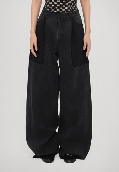 Wide-leg black denim pants with contrasting black fabric panels at the sides, featuring a high waist and a relaxed fit.