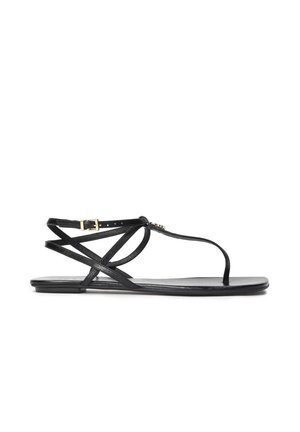 Sandalia de cuero negro con tiras delgadas que se cruzan sobre el pie y alrededor del tobillo. Cuenta con una pequeña hebilla dorada. Suela plana.