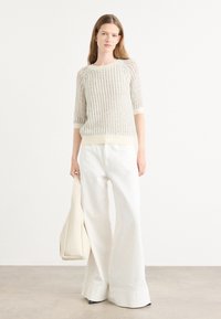 Beige gebreid sweater met een textuurpatroon, driekwart mouwen en een lichtgekleurde tailleband. Gecombineerd met brede witte broek en een beige tas.