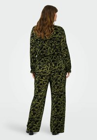 Černý a zelený vzorovaný outfit s dlouhými rukávy a širokými kalhotami. Texturovaná látka s žebrovaným povrchem. Design obsahuje abstraktní tvary.