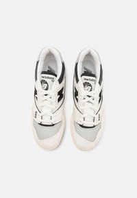 Sneakers blancs et gris avec une tige en mesh et en daim, présentant des accents noirs sur les côtés et les lacets. Semelle en caoutchouc avec un motif texturé.