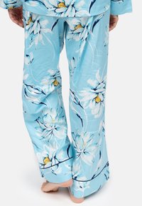 Jasnoniebieskie spodnie piżamowe z dużym kwiatowym wzorem w bieli i żółci. Wykonane z gładkiego materiału, charakteryzujące się luźnym, swobodnym krojem.