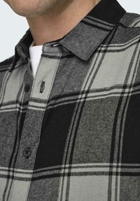Grijze en zwarte geblokte shirt met een knoopkraag, voorzien van een gestructureerde stof, zichtbare stiksels en een borstzak met knoopdetail.