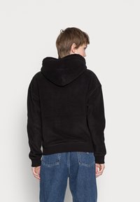 Felpa nera con cappuccio dal tessuto morbido, caratterizzata da una vestibilità comoda e polsini a coste, abbinata a jeans blu a vita alta.