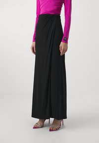 Maxi gonna nera con design drappeggiato, realizzata in tessuto morbido. Abbinata a una maglietta a maniche lunghe di un vivace rosa e sandali con tacco rosa con accenti trasparenti.