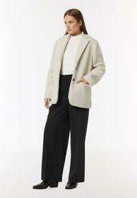 Cream, faux fur blazer with a straight cut, notched lapels, and two front pockets, paired with black wide-leg trousers and heeled boots.