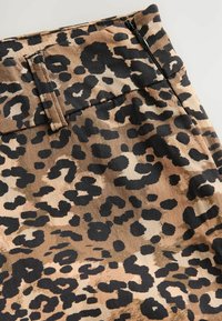 Tissu à imprimé léopard en tan et noir avec une texture lisse. Comprend une taille élastique et une fermeture éclair pour un enfilage facile.