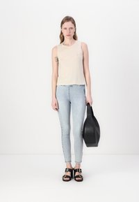 Beige ermeløs topp, lyseblå smale jeans, svart håndveske, og svarte sandaler med spenner. Enkel design og uformell utseende.