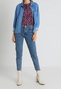 Jeansjacka över en rosa leopardmönstrad topp, kombinerad med ljusblå jeans och beige ankelboots. Outfiten har olika texturer och mönster.