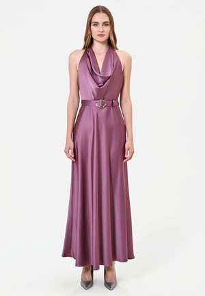Donna che indossa un vestito senza maniche in raso malva con scollo a cappuccio, vita cintata e tacchi appuntiti argentati su sfondo bianco uniforme.
