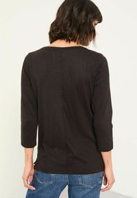 Black, long-sleeve top with a scoop neckline and casual fit. Fabric has a slight texture, featuring a central seam at the back.