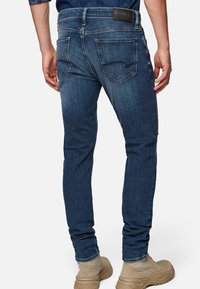 Dark blue denim jeans with a slim fit, featuring a branded leather patch, two back pockets, and subtle fading on the thighs.