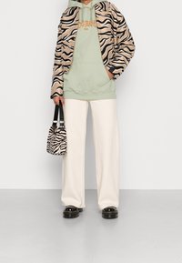 Chaqueta bomber de estampado de cebra sobre una sudadera verde menta, combinada con pantalones de pierna ancha color crema y un pequeño bolso de estampado de cebra. Zapatos con plataforma gruesa.