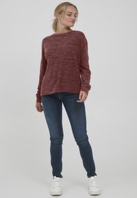 Bordeaux langermet genser med melert tekstur, avslappet passform og rund hals, kombinert med mørke skinny jeans og hvite sneakers.