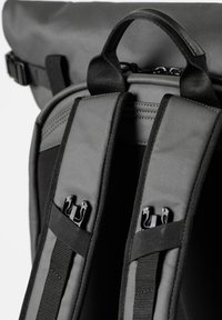 Zaino nero con doppie spalline imbottite, dotato di clip in metallo nero e cuciture testurizzate. Chiusura a risvolto visibile nella parte superiore.