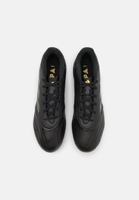 Zapatillas deportivas negras de cuero suave con punta redondeada, que presentan acentos texturizados y cordones centrales. Detalle de marca dorada visible.