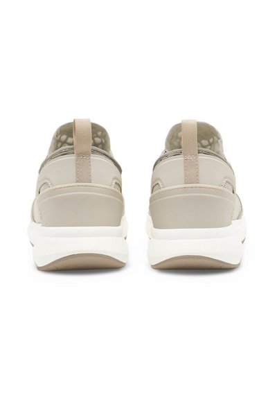 Baskets beiges avec une tige lisse en synthétique, semelle blanche contrastante et languettes arrière. Doublure texturée visible à travers les sections en maille.