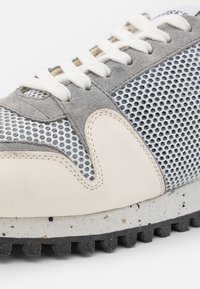 Gros plan d'une basket grise et blanche avec tissu en mesh, suède, panneaux en cuir cousu, lacets blancs et semelle noire robuste.
