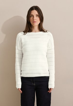 Pull en tricot blanc avec un motif texturé et rayé, un col rond et des manches longues ; associé à un jean en denim foncé.