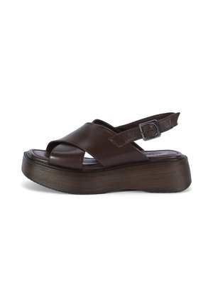 Donkerbruine leren platformsandalen met gekruiste bandjes en een verstelbare enkelriem met gesp op een witte achtergrond.
