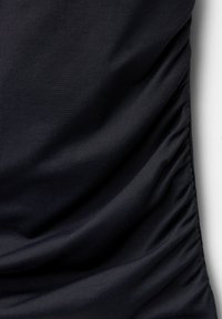 Tissu noir avec une fine texture côtelée et un détail de fronces rassemblées le long du côté droit créant des plis doux.