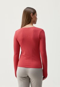 Długi rękaw w kolorze koralowym, z dopasowanym krojem, prążkową teksturą na rękawach oraz subtelnym otwartym tyłem. Połączony z jasnoszarymi, fakturowanymi spodniami.