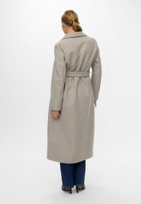 Lungo cappotto grigio realizzato in tessuto morbido, dotato di una cintura, colletto a rever e maniche lunghe, visto da dietro.