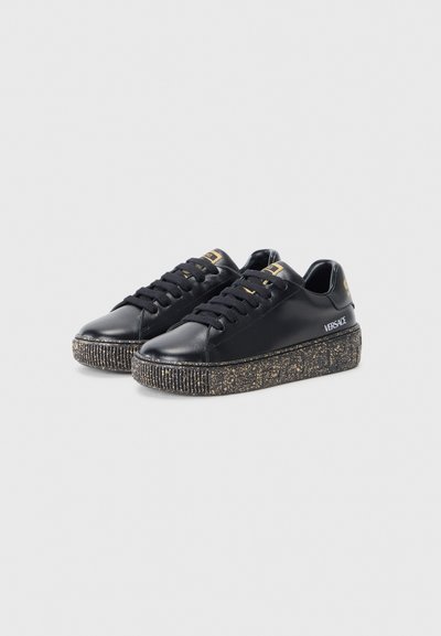 Zapatillas de cuero negro con una suela de plataforma negra texturizada y brillante. Presentan cordones negros, detalles en dorado y un diseño de punta redondeada.
