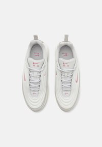 Valkoiset urheilukengät, joissa on vaaleanpunaisia yksityiskohtia, sileä kangaspinta, tekstuuriset sivut, pyöreät kuviot ja korostunut kantatappi.