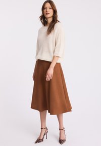 Beżowy sweter dzianinowy z krótkimi rękawami, w połączeniu z brązową spódnicą w kształcie litery A i szpilkami w cętki, na tle białego tła.