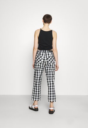 Czarny top na ramiączkach i czarno-białe, szerokie spodnie w kratę z wysokim stanem, z widocznymi kieszeniami i postrzępionymi lamówkami, zestawione z białymi sandałami.