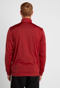Chaqueta deportiva roja con cuello alto, hecha de un material suave y ligero, que presenta mangas largas y un diseño ajustado.
