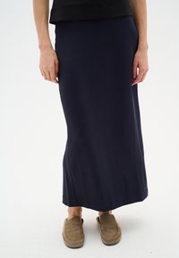 Mornarica, kratka suknja do članka napravljena od glatkog, rastezljivog materijala. Ima prilagođen struk i suptilan popravljeni oblik. Nošena sa bež papučama.