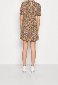 Luftig kort klänning med svart botten, prydd med gula och lila blommönster. Puffärmar och en nyckelhålsdetalj i ryggen. Matchad med vita sneakers.