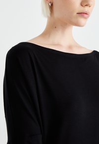 Black, off-the-shoulder top with a relaxed fit, made from soft fabric. Smooth texture, minimal stitching, and short sleeves.