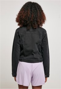 Zwarte denimjack met een getailleerd ontwerp, knopenmanchetten en twee achterzakken. Gekozen boven lichtlavendel korte broek van een gestructureerde stof.